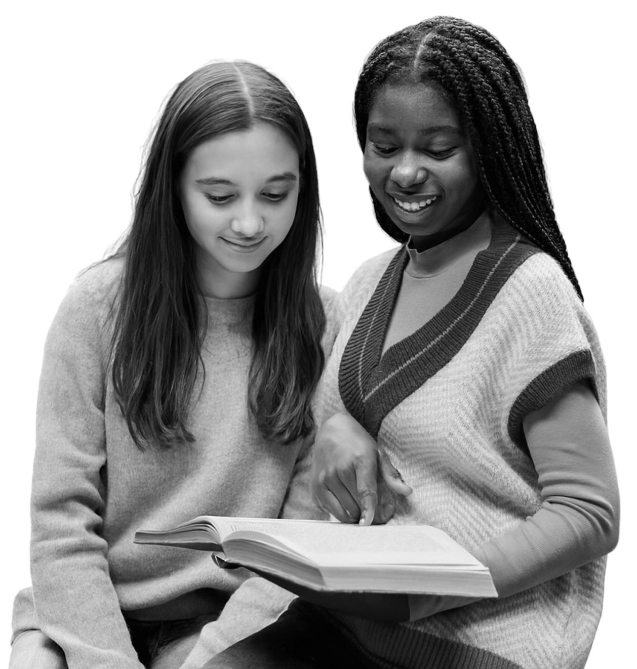 Two young women sitting together and reading a book, one pointing at the text and both smiling.